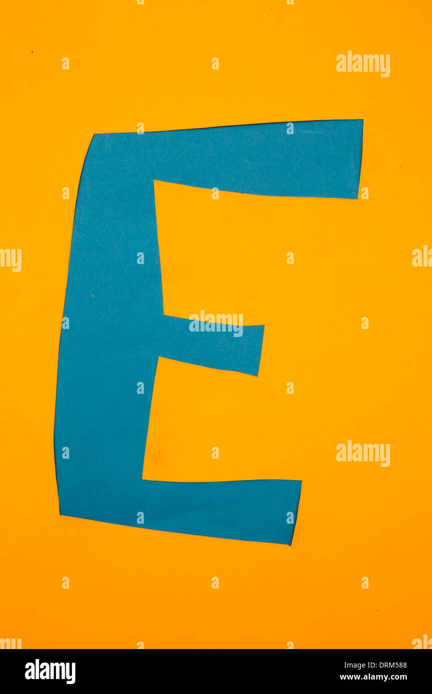 Letter 'E' cut out of blue paper at yellow background, studio shot Stock Photo