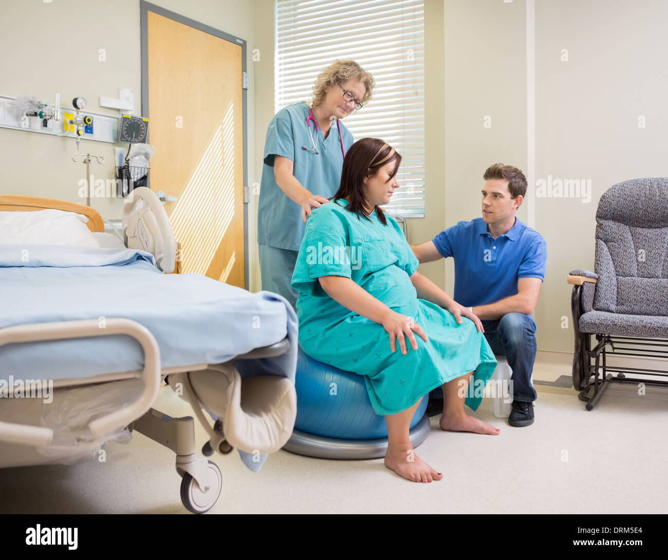 Nurse And Man Assisting Pregnant Woman On Exercise Ball Stock Photo