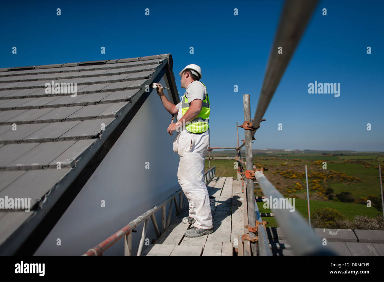 A construction worker painting facia boards on a new build house, Madron, Cornwall, UK Stock Photo