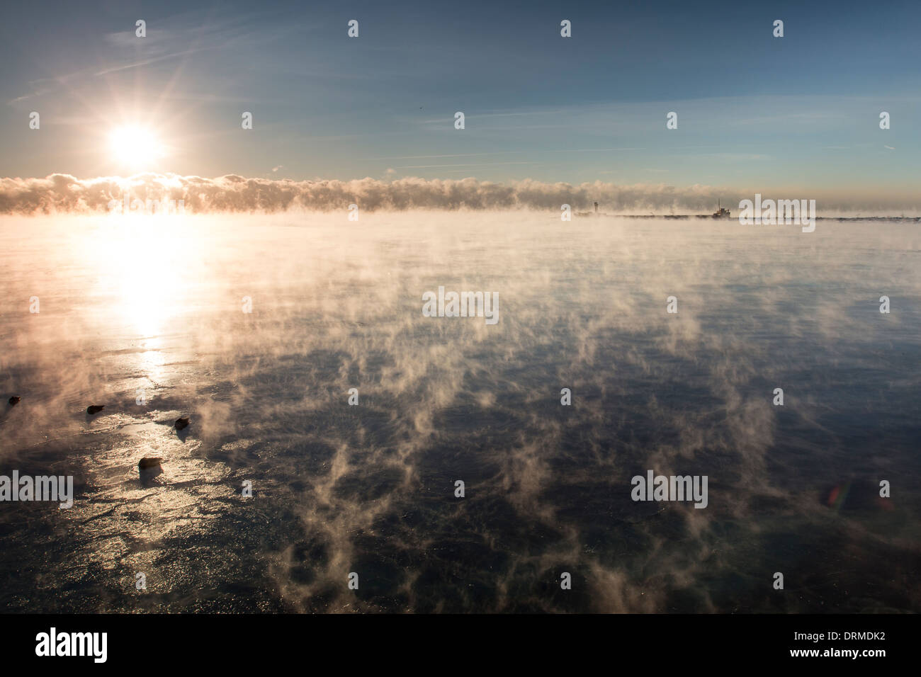 The sun rises above a band of lake effect cloud and the steaming waters of Lake Ontario under a frigid polar weather airmass Stock Photo