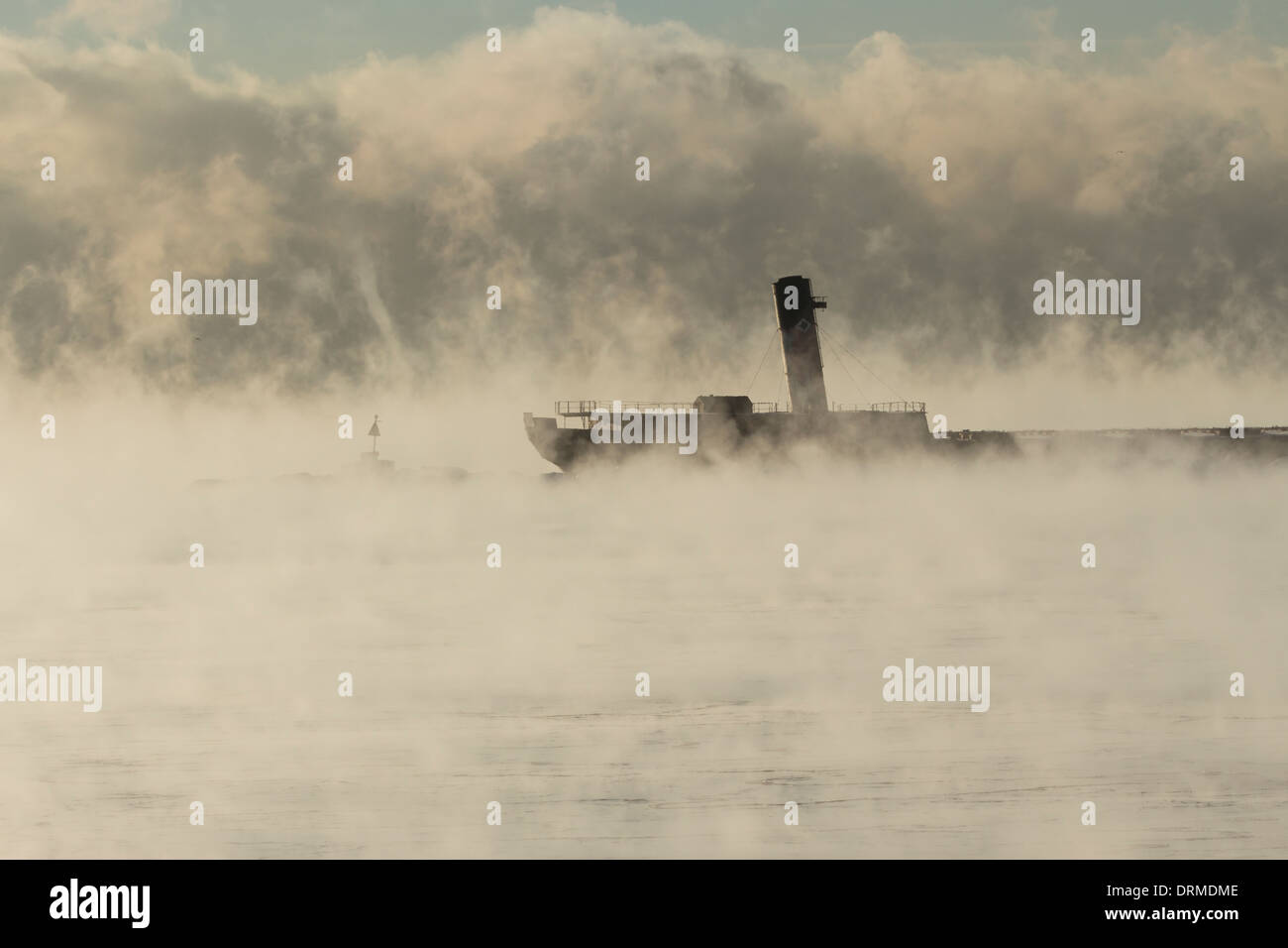A ship stands in port amidst the steaming waters of Lake Ontario as a steam devil vortex dances in the distance Stock Photo