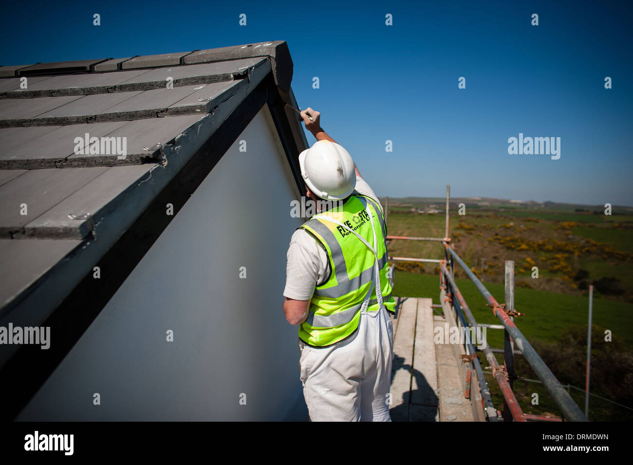 A construction worker painting facia boards on a new build house, Madron, Cornwall, UK Stock Photo