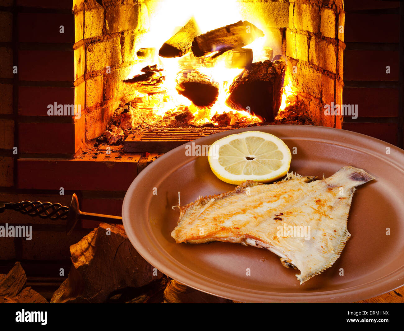 fried sole fish on plate and open fire in wood burning oven Stock Photo