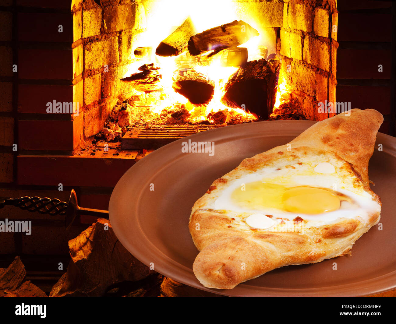 adzharia hachapuri with egg on plate and open fire in wood burning stove Stock Photo