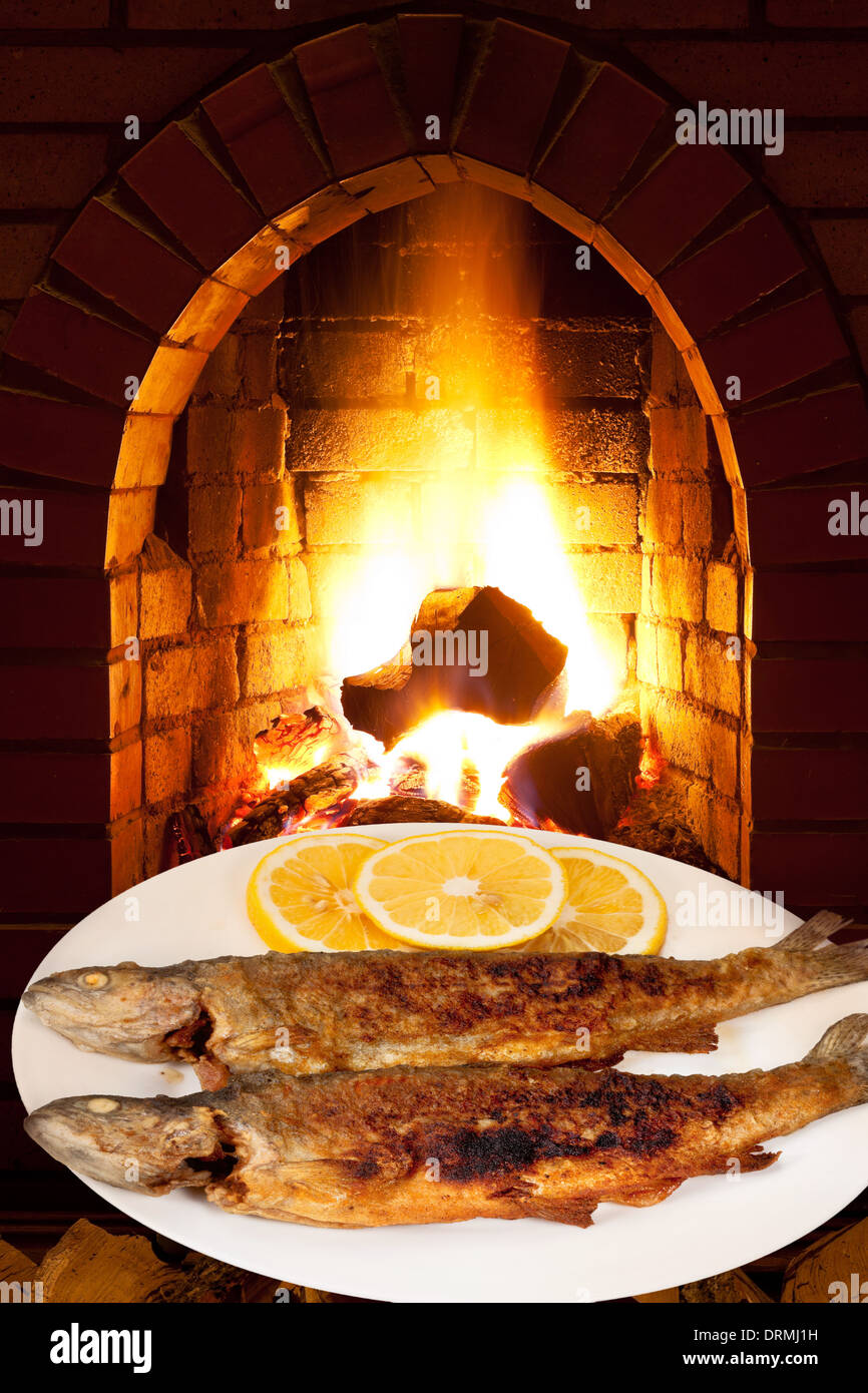 fried trout fish on white plate and open fire in wood burning oven