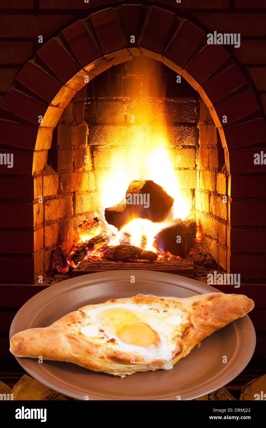 adzharian khachapuri with egg on plate and open fire in wood burning stove Stock Photo