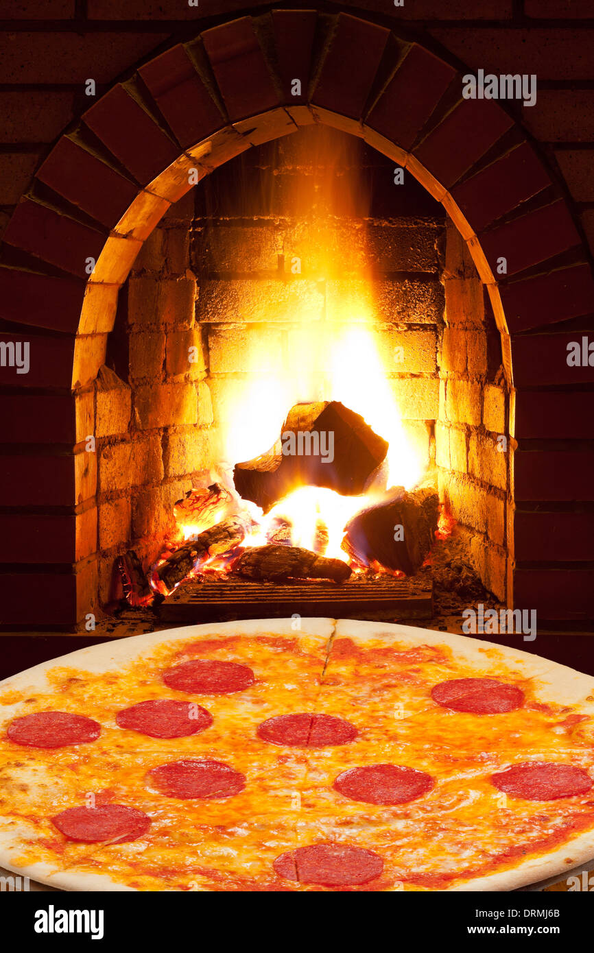 italian pizza with sausage and open fire in wood burning oven Stock Photo