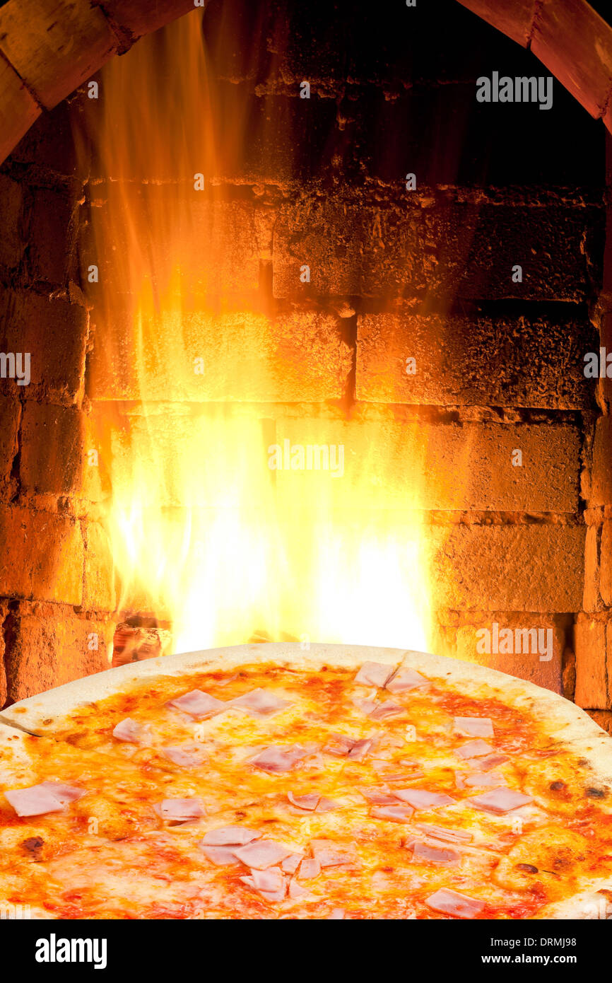 italian pizza with prosciutto cotto and fire flames in wood burning oven Stock Photo