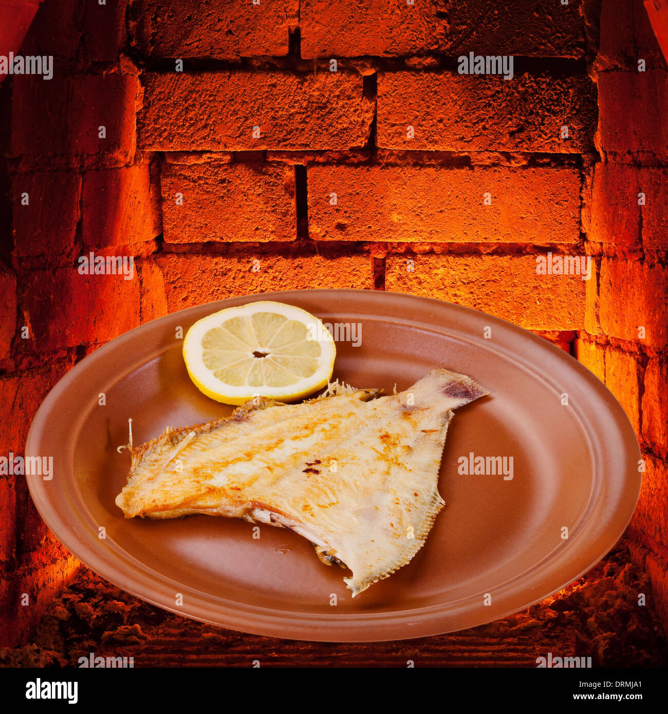 fried sole fish on plate and hot bricks of wood burning oven Stock Photo