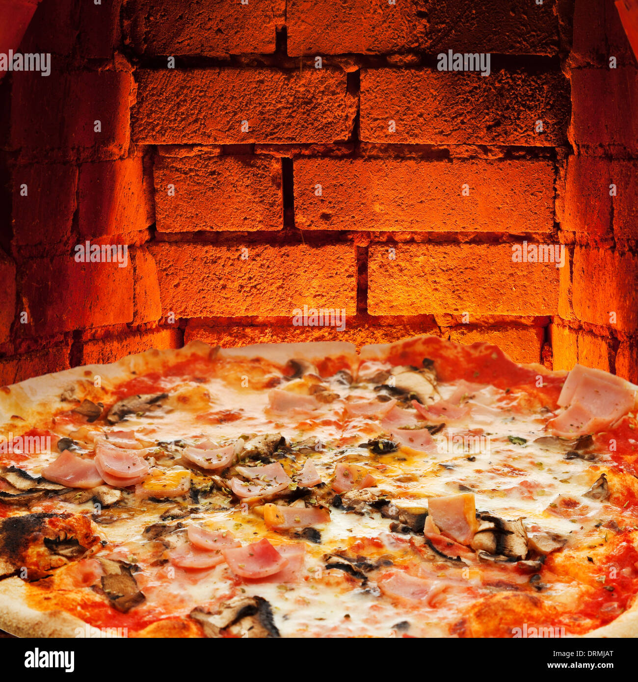 italian pizza with ham and mushrooms and hot brick wall of wood burning oven Stock Photo