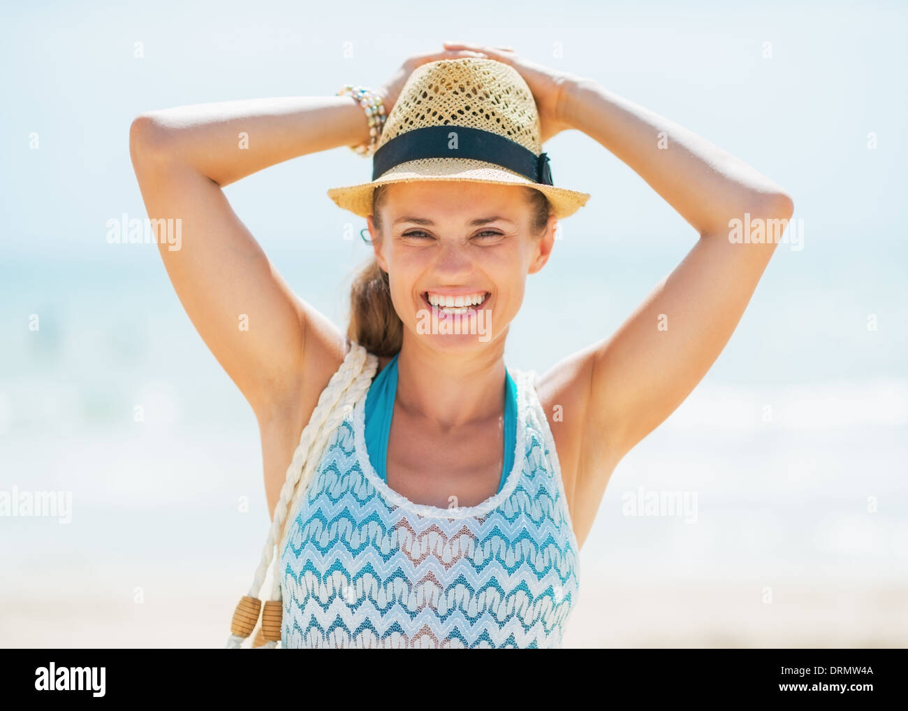 Portrait of smiling young woman in hat and with bag on beach Stock Photo