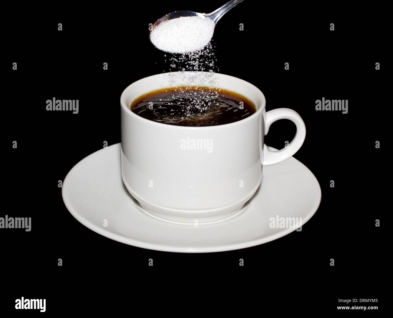 Sugar is poured from a spoon into a cup of coffee isolated on a black background Stock Photo