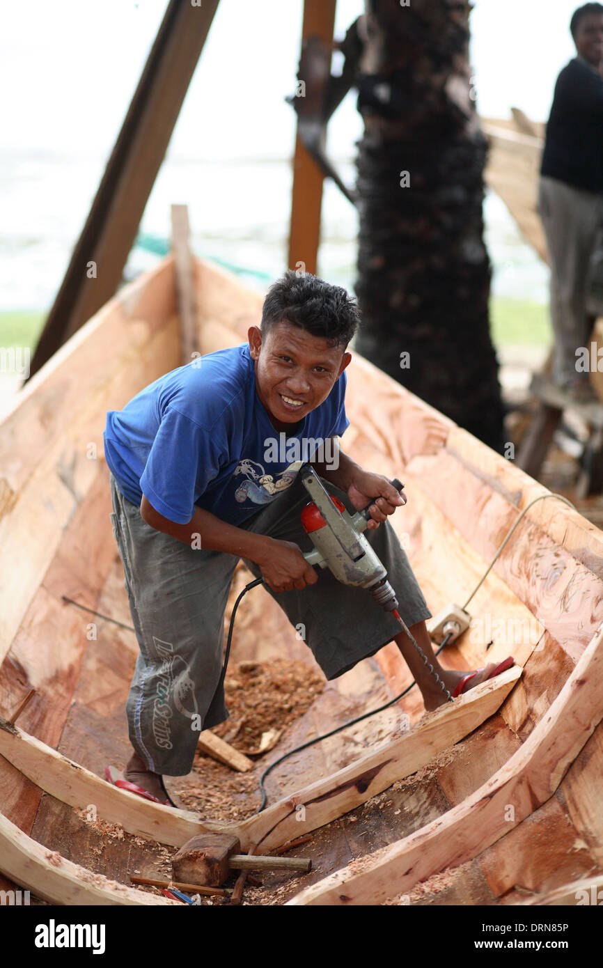Portrait of smiling Indonesian young man drilling holes and building a wooden boat Kupang, West Timor, Indonesia Nov 2005 Stock Photo