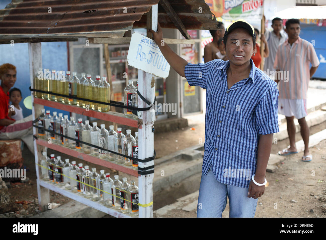 A smiling young man sells gasoline / petrol in bottles along the side of the road. Kupang, West Timor, Indonesia Stock Photo