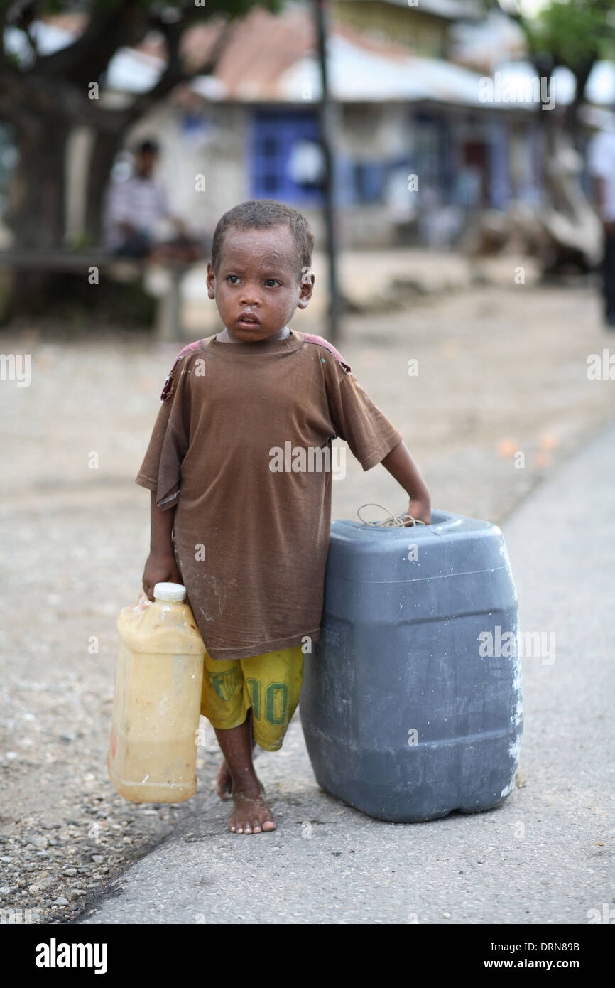 Small boy standing by road holding a jug and by a plastic container Kupang, West Timor, Indonesia. Stock Photo