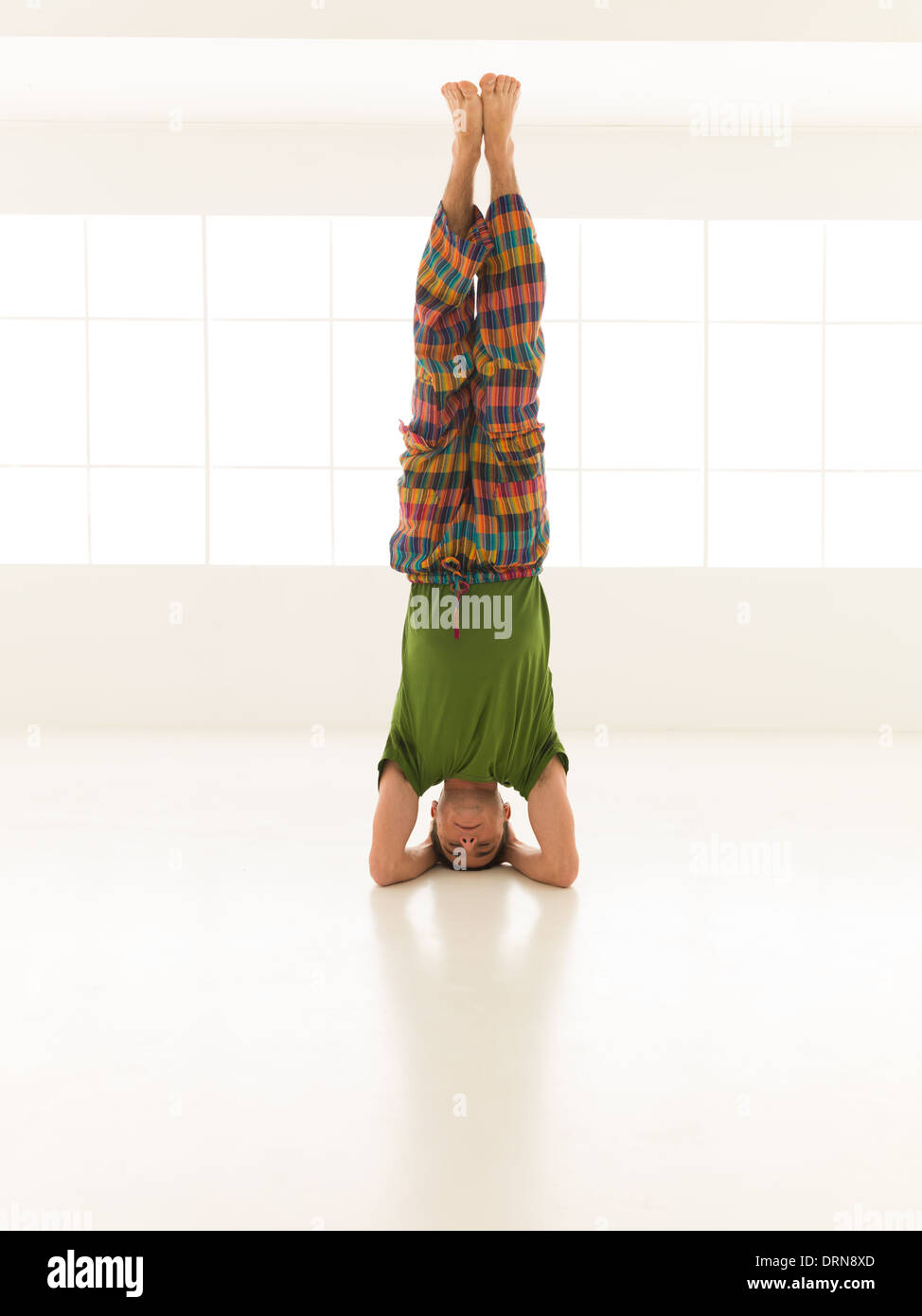 close up of single young man in advanced yoga posture, dressed colorful, in studio gym Stock Photo