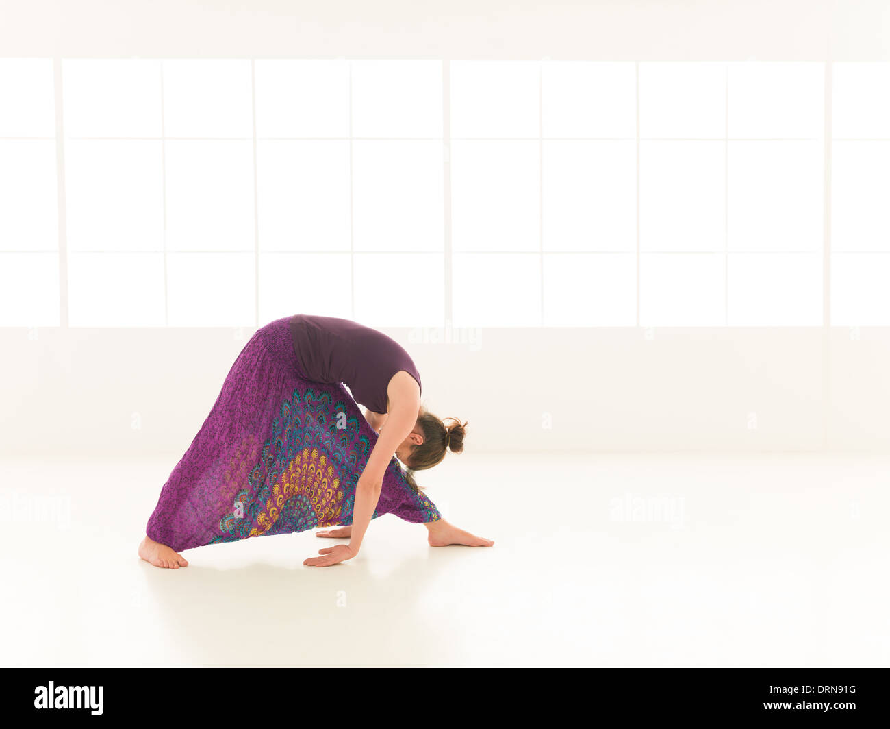 side view of young woman in yoga posture, face obscuredm dressed colorful, iluminated window backgrond Stock Photo
