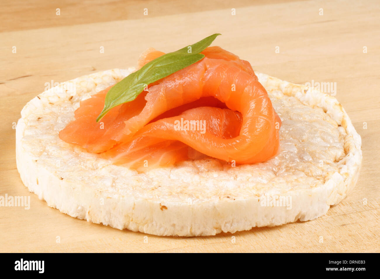 Close-up of a rice cake with smoked salmon and basil, over a wooden background. Stock Photo