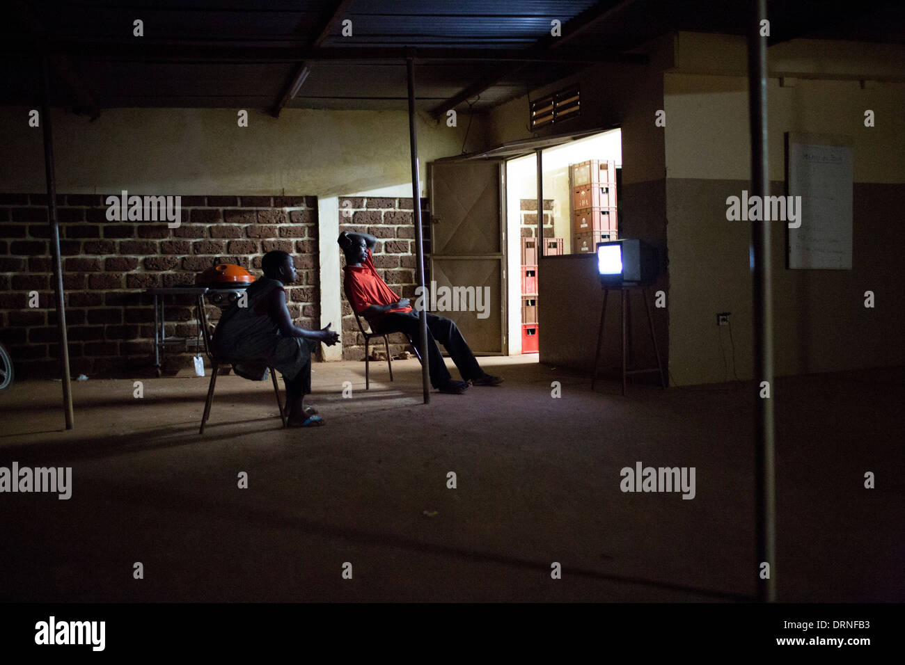 young men sit outside bar in Burkina Faso watching tv Stock Photo