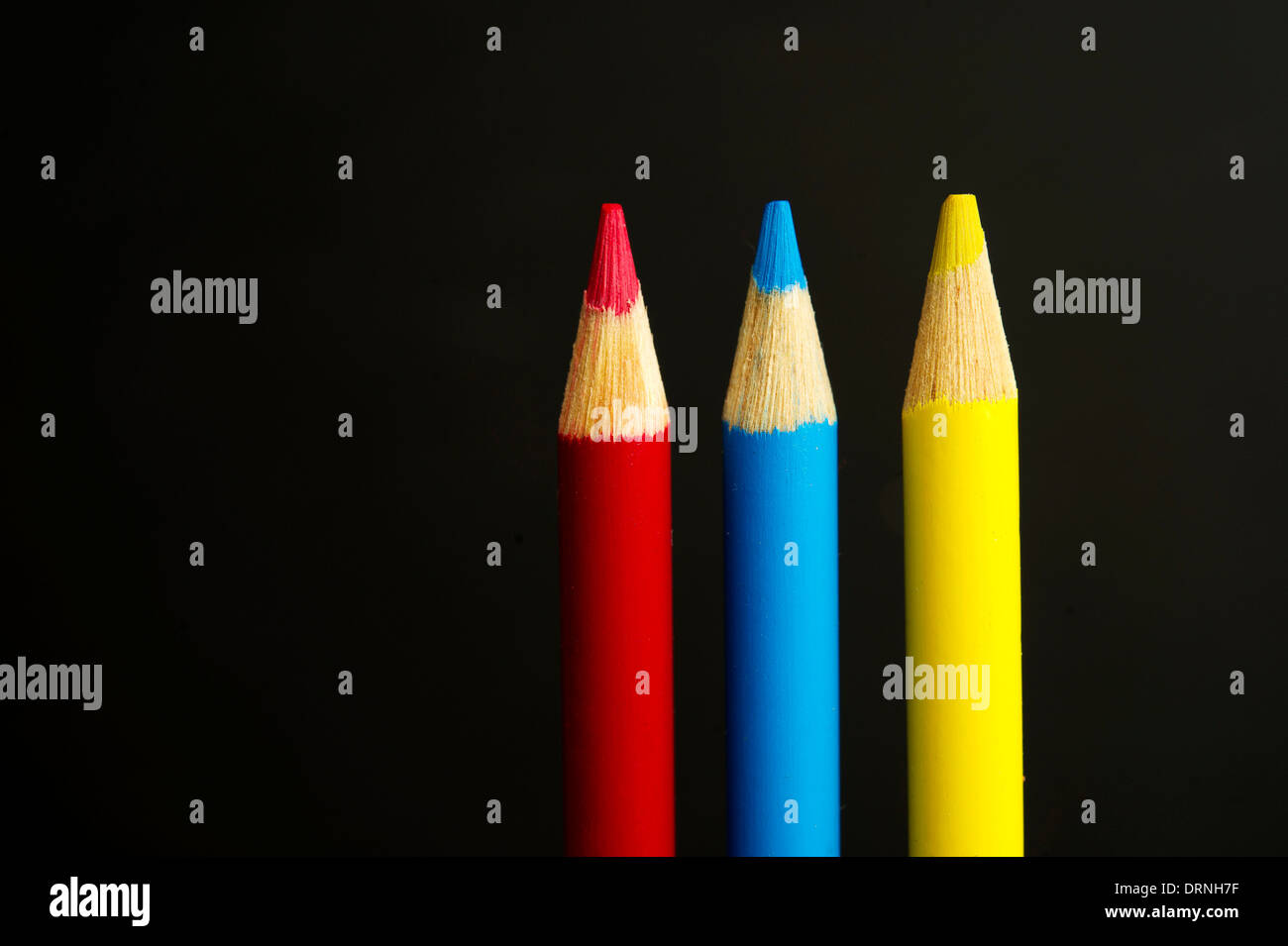 Children's red, blue and yellow coloured pencil crayons on a black background Stock Photo