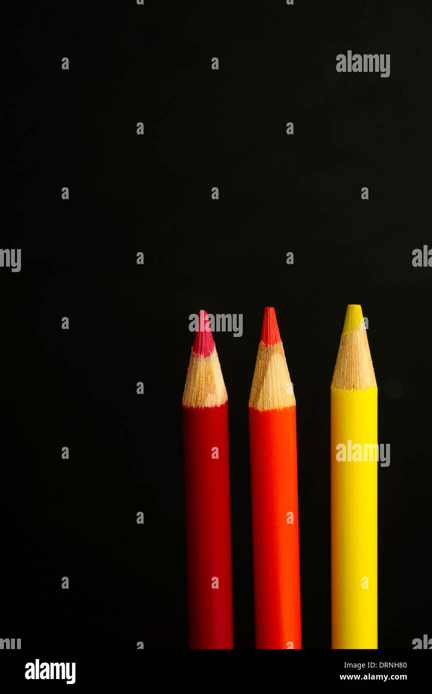 Children's red, orange and yellow coloured pencil crayons on a black background Stock Photo