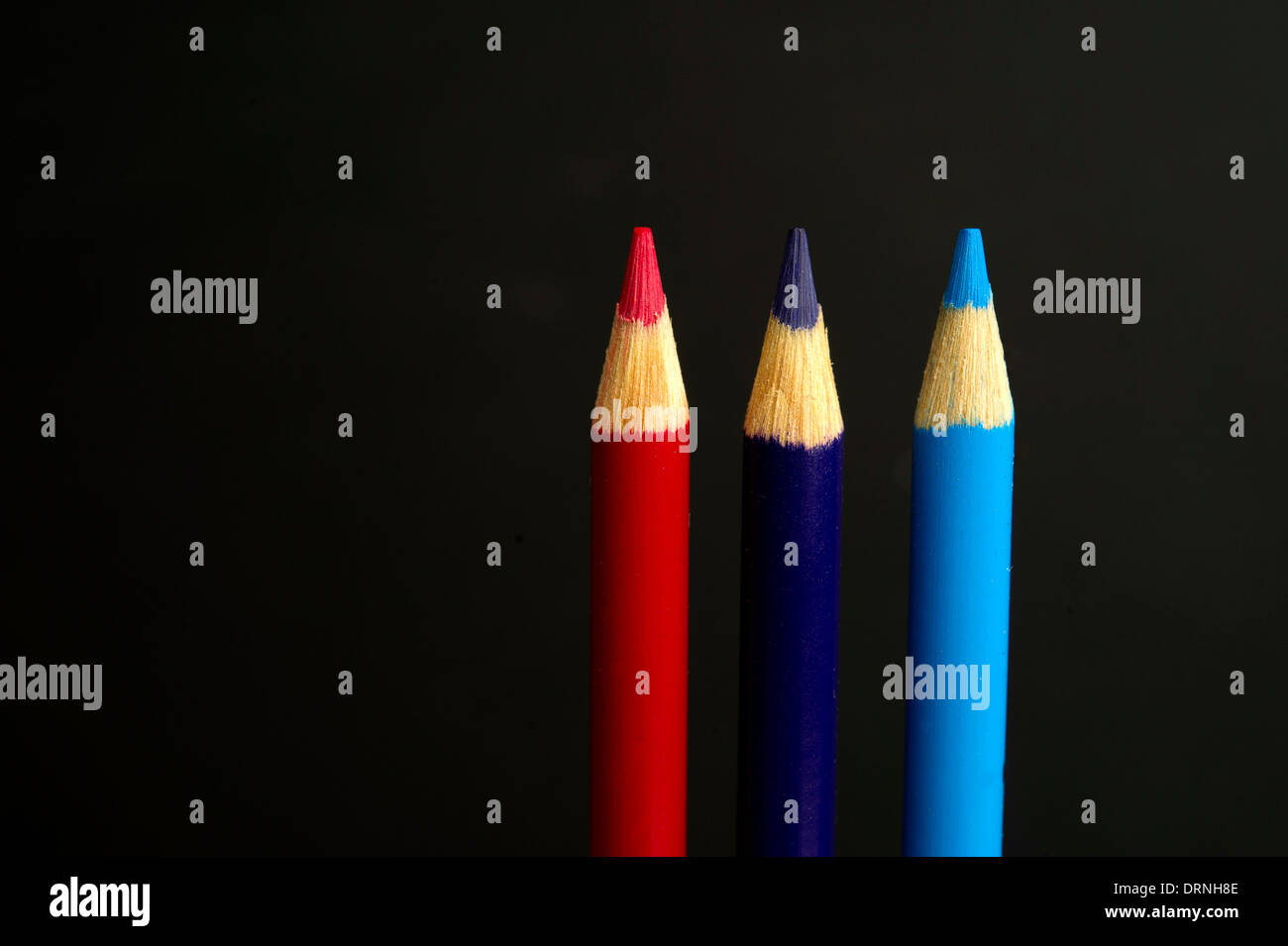 Children's red, purple and blue coloured pencil crayons on a black background Stock Photo