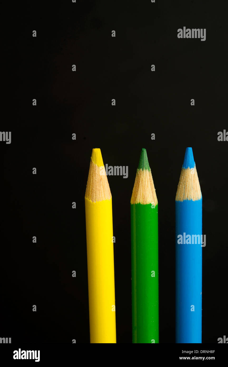 Children's yellow, green and blue coloured pencil crayons on a black background Stock Photo