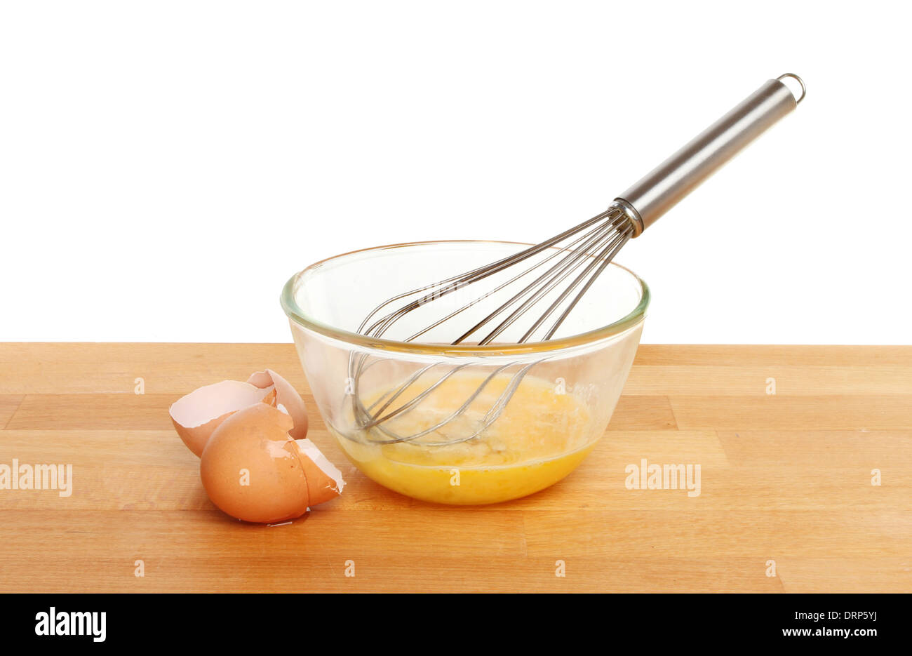 Cracked eggs with a whisk in a glass mixing bowl on a kitchen worktop against a white background Stock Photo