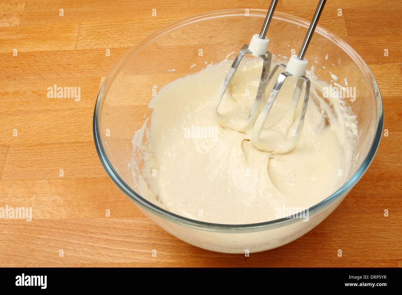 Cake mix in a glass mixing bowl with a whisk on a wooden worktop Stock Photo