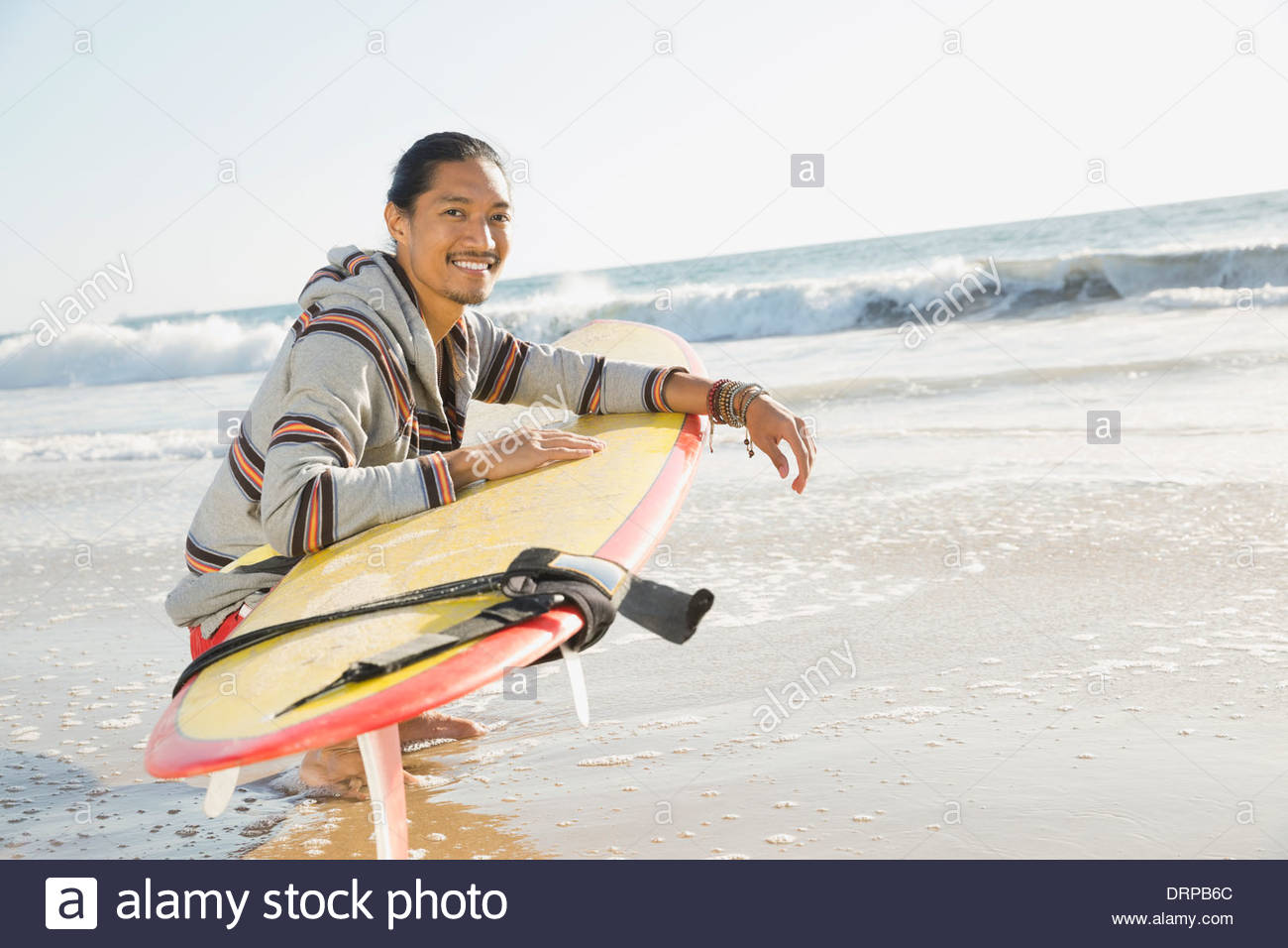 Portrait of man with surfboard crouching on beach Stock Photo