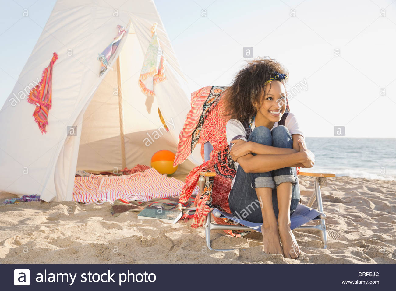 Smiling woman hugging knees by tent on beach Stock Photo