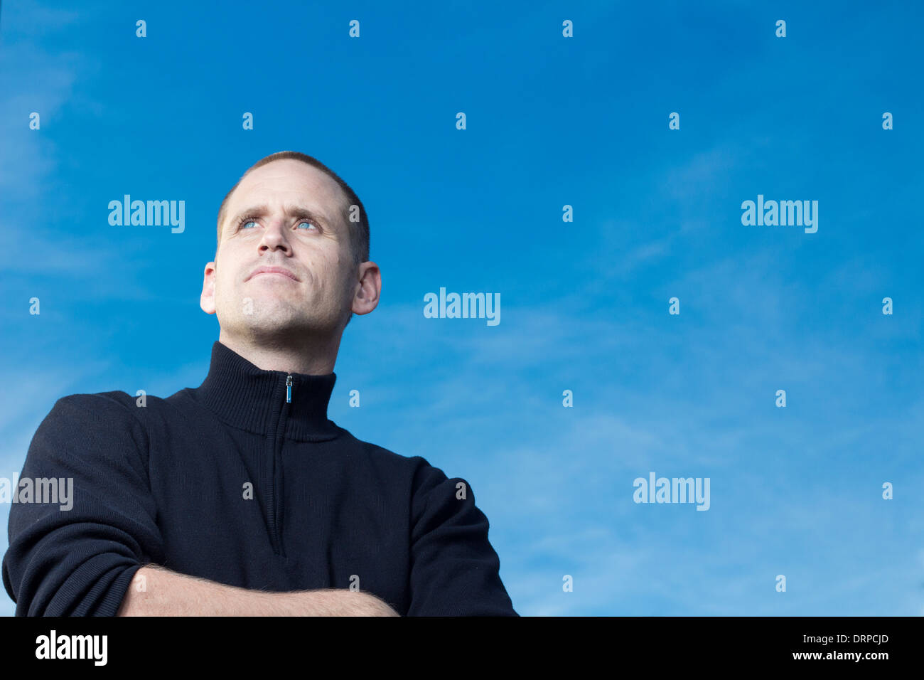 An athletic man is gazing into the distance against a blue sky. Stock Photo