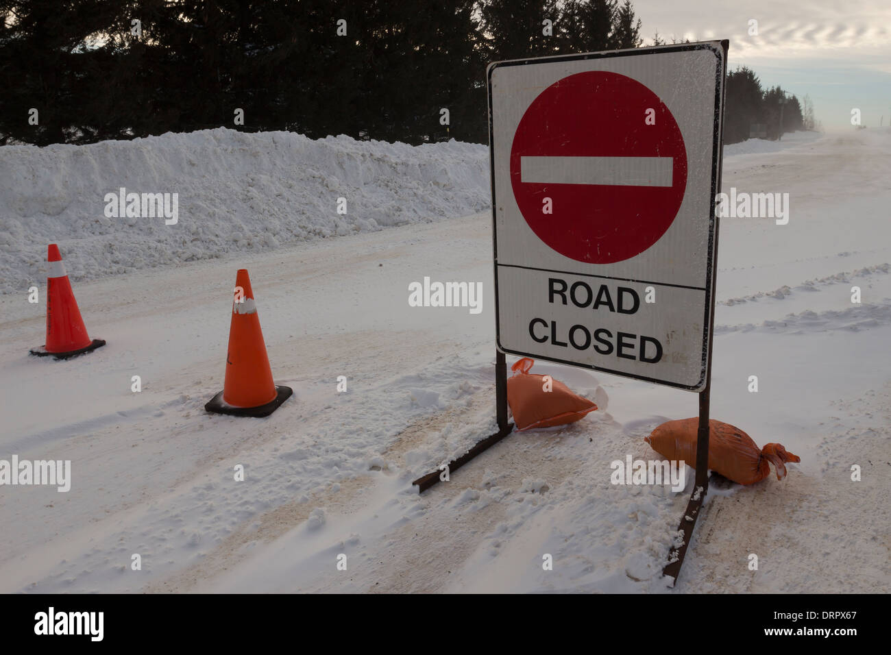 A road closure sign blocks a roadway after vehicles become trapped in wind blown winter snow & severe winter blizzard conditions Stock Photo