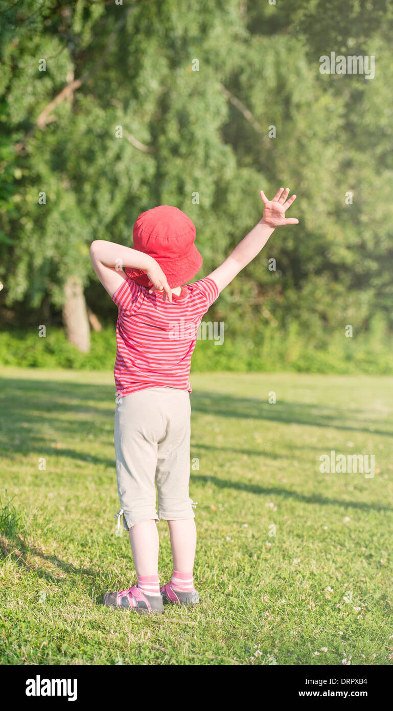 Tranquil summer scene. Young girl in green park making gesture with raised arms. Stock Photo