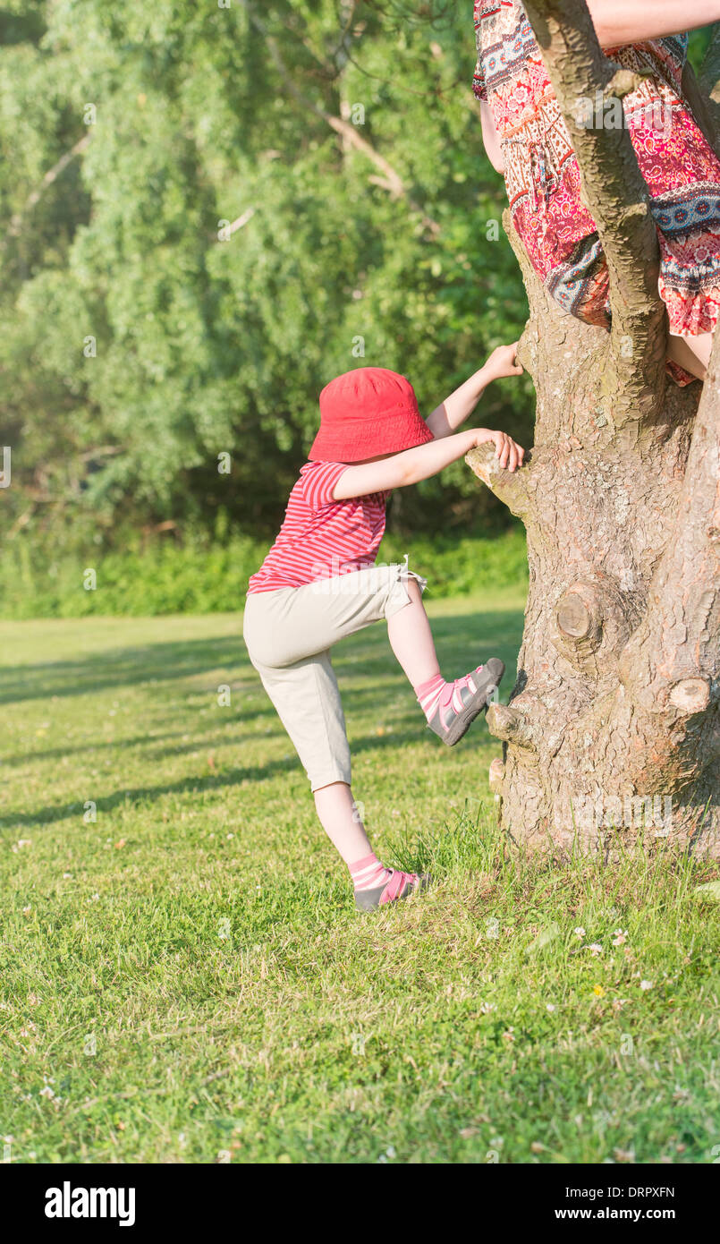 Tranquil summer scene. Young girl in green park climbing with mother up in the tree. Stock Photo