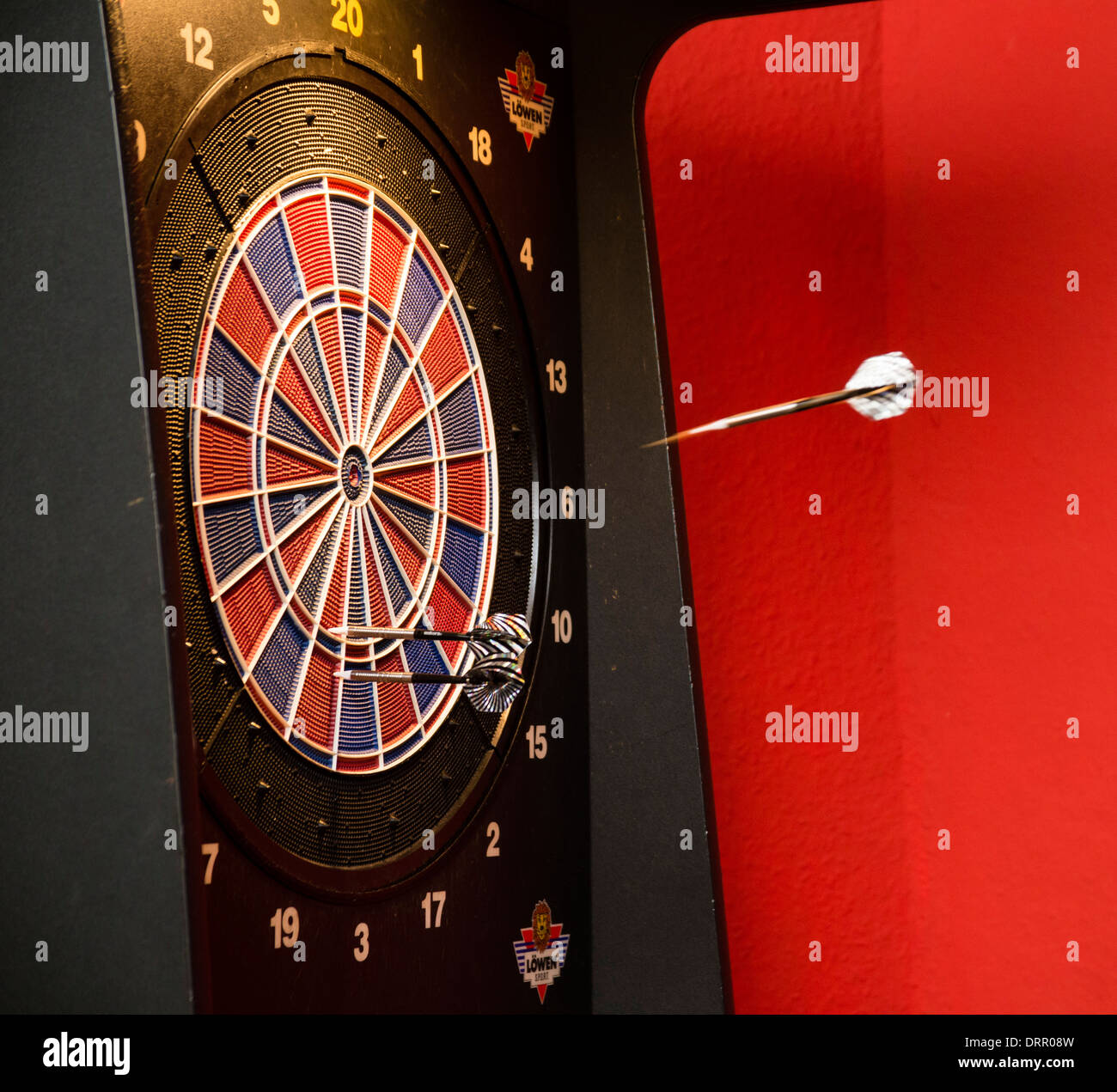 Darts are flying towards the dart board in a pub. Stock Photo