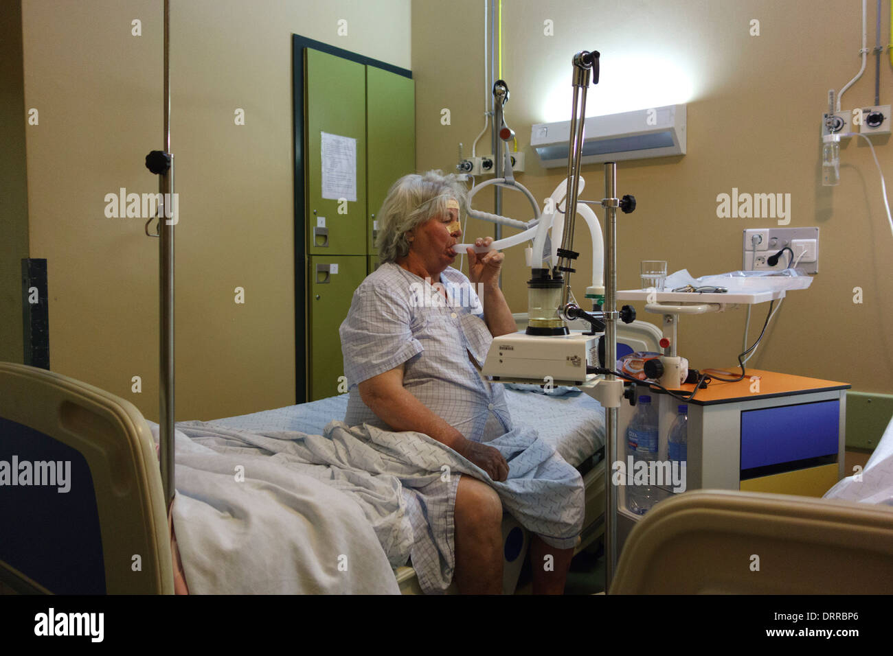 Patient using automatic mucus suction pump while sitting in a hospital bed Stock Photo