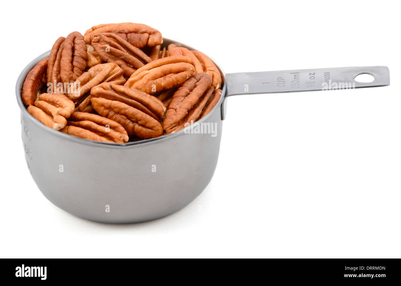 Whole pecan nuts in a metal cup measure, isolated on a white background