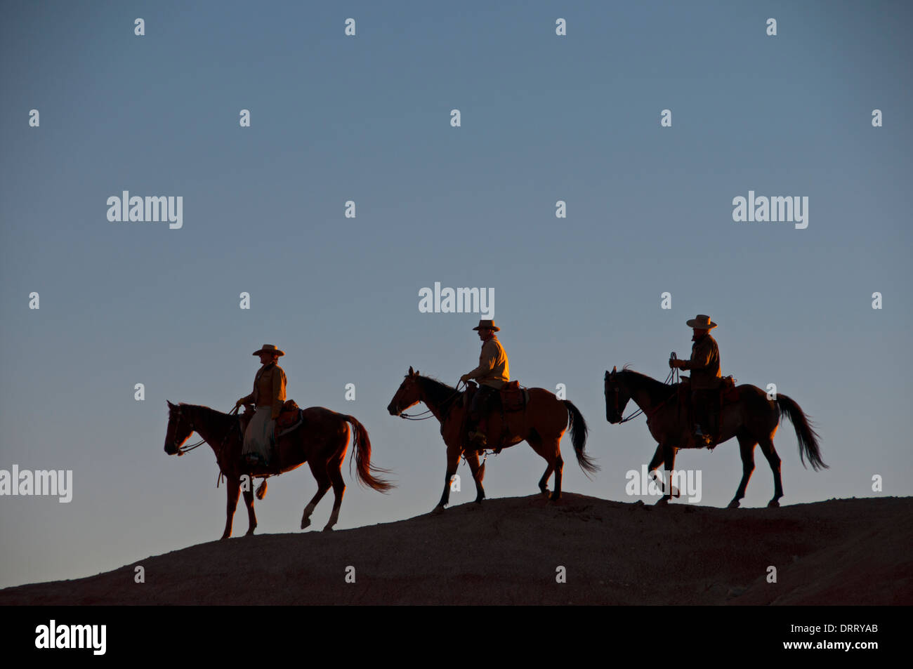 Three silhouetted wranglers on horseback after completing a horse round-up in  Painted Hills of the Bighorn Mountains, Wyoming Stock Photo