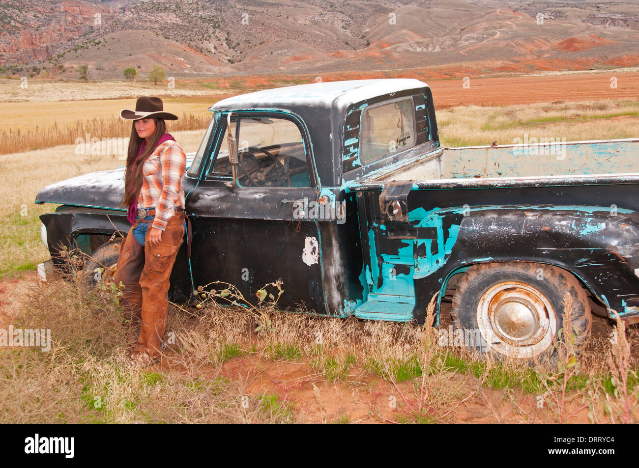 Attractive cowgirl stands beside an old Dodge truck before a horse round up in the Bighorn Mountains on Wyoming Stock Photo