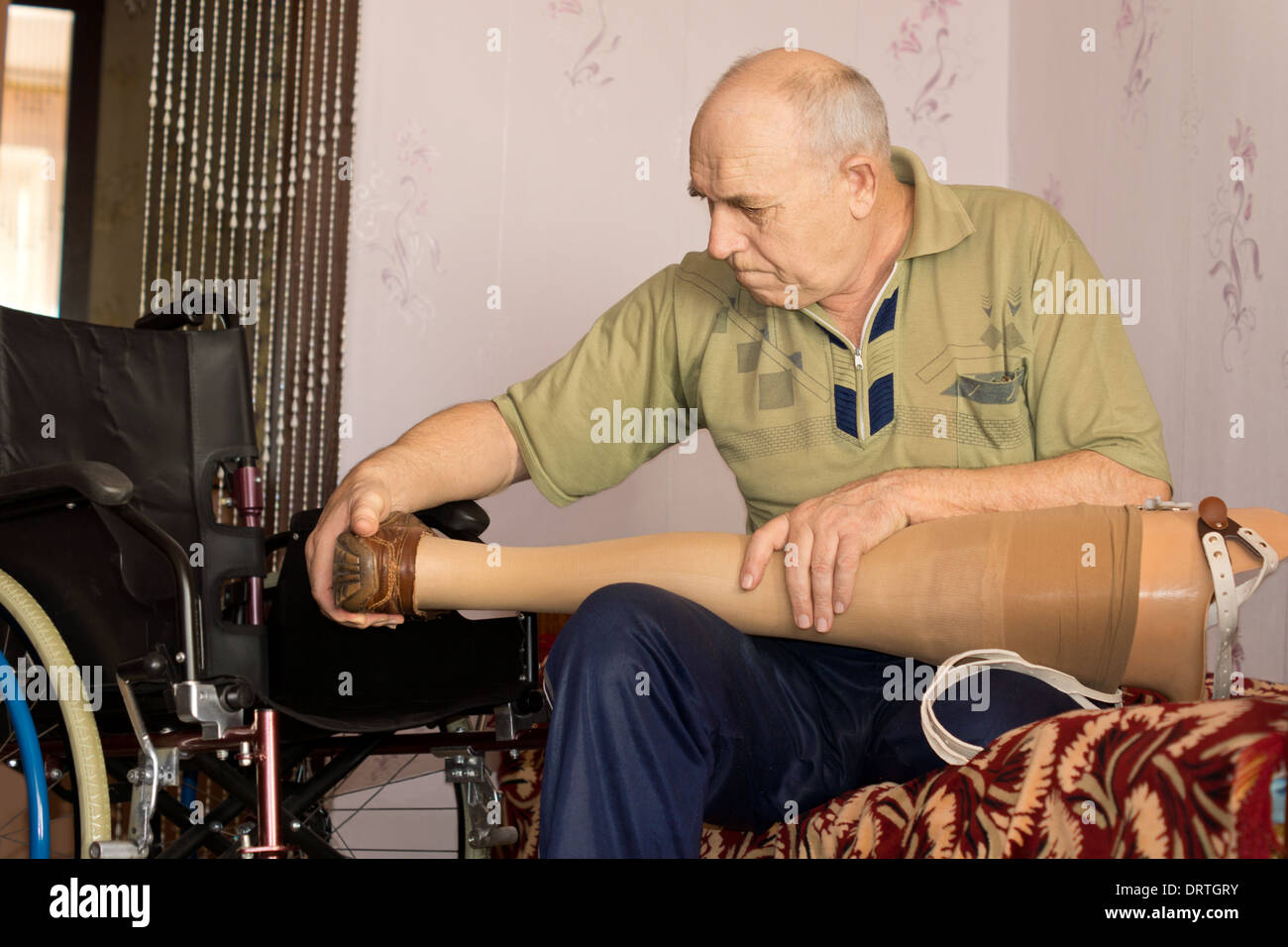 Senior man sitting on his bed checking out his artificial leg before fitting it to his stump following an amputation Stock Photo