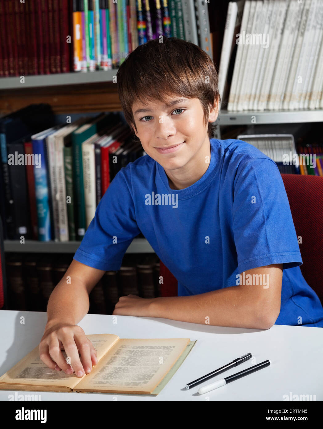 Teenage Schoolboy Smiling While Sitting In Library Stock Photo