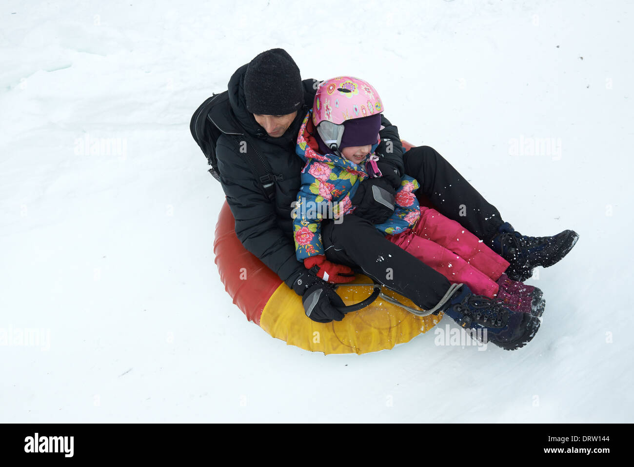 Father and daughter having fun in snow inner tube snowtubing Stock