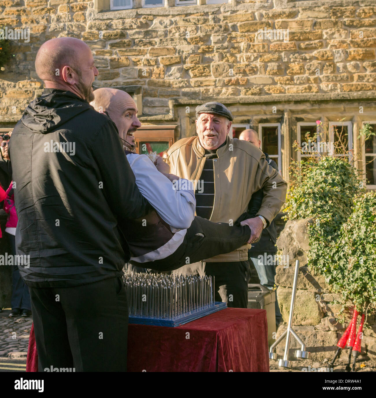 Street Entertainer being placed on a bed of nails by members of the audience  at the Grassington Dickensian Festival, 2013. Stock Photo
