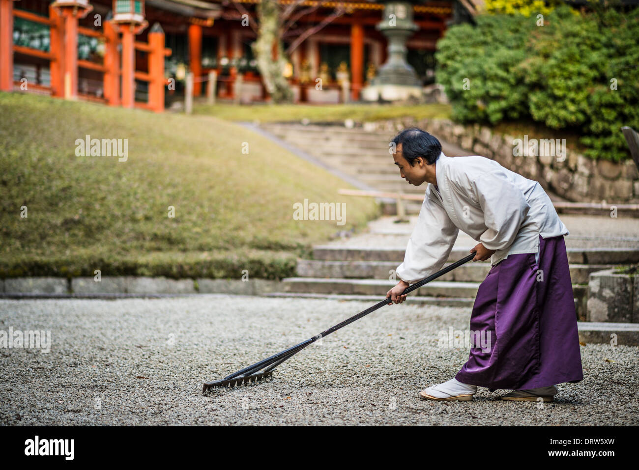 Japanese Shinto priest rakes a rock garden. Stock Photo