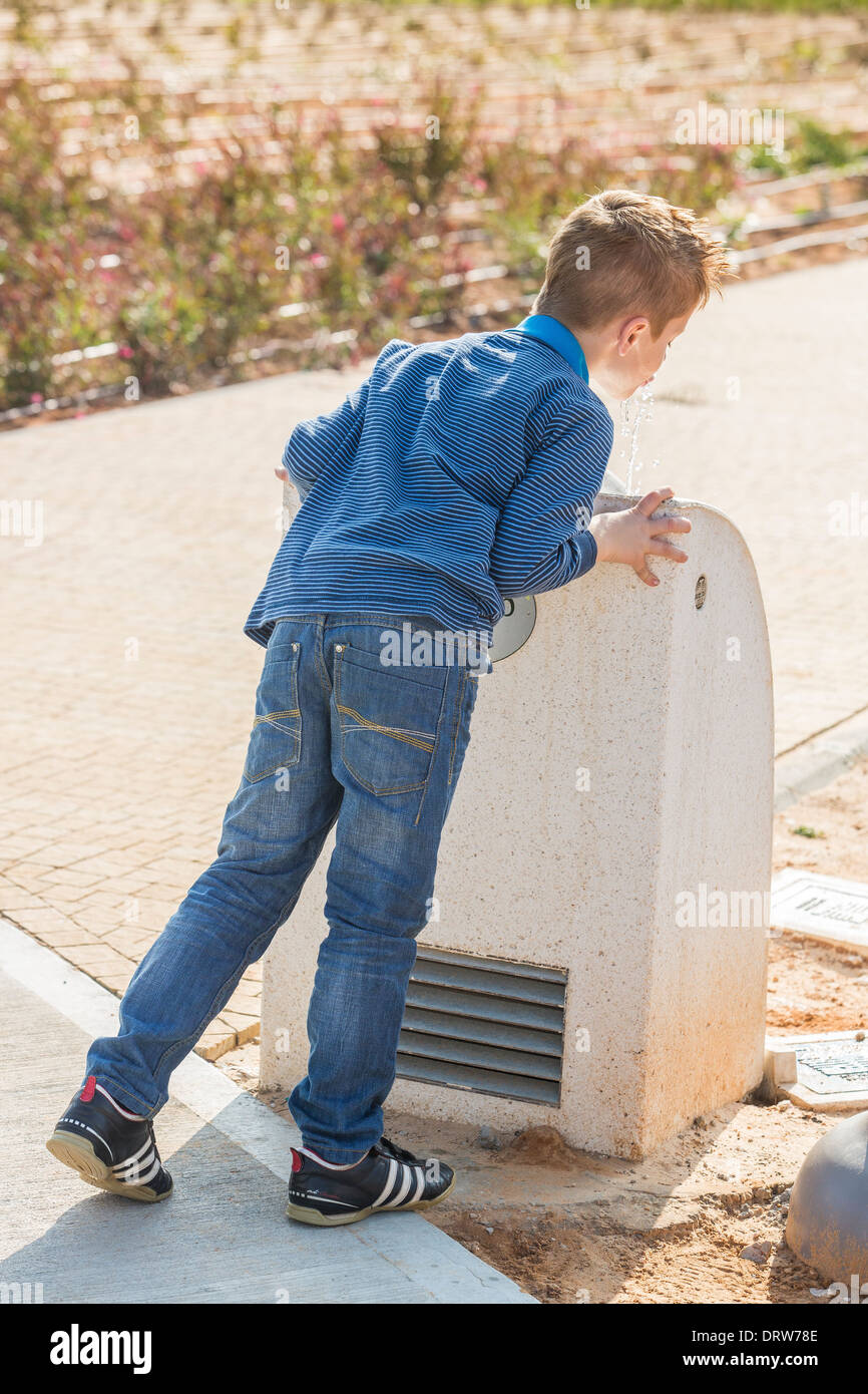 young, red haired boy drinks water from a drinking fountain Stock Photo