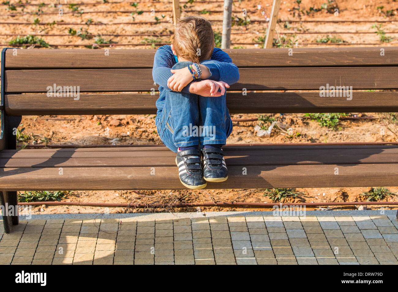 Young depressed red haired boy alone on a bench in a park Stock Photo