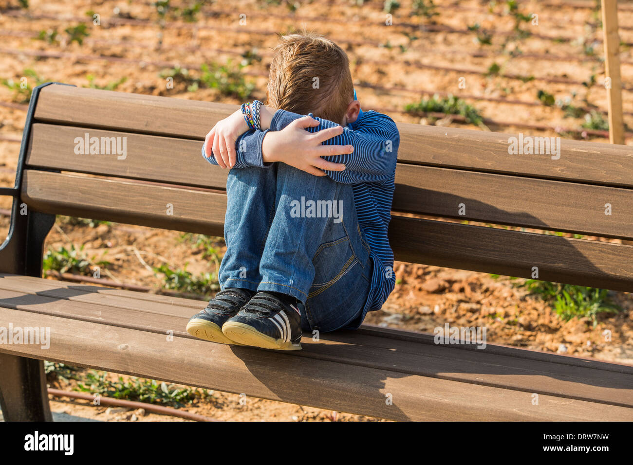 Young depressed red haired boy alone on a bench in a park Stock Photo