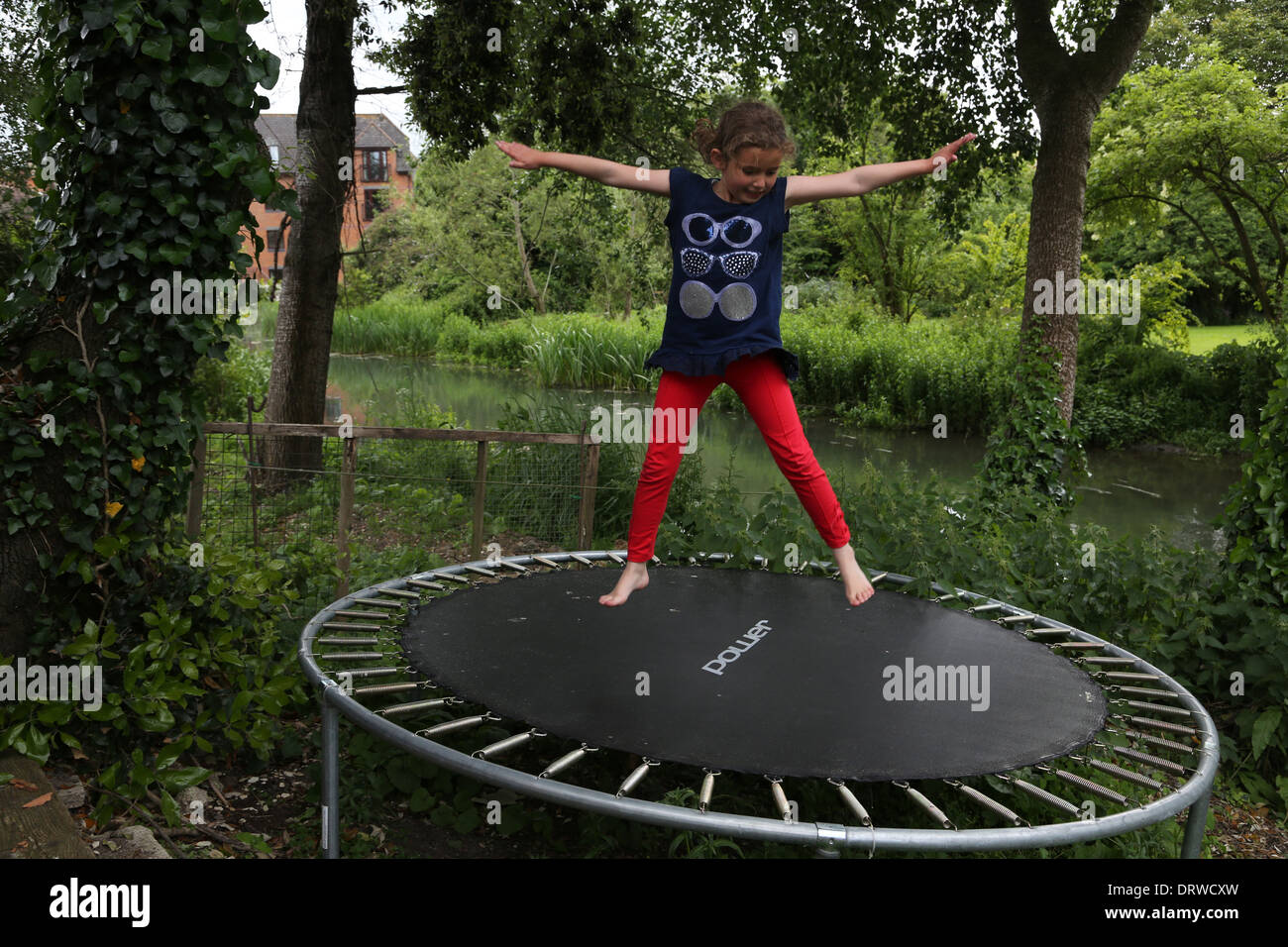 Young Girl Doing Star Jumps On A Trampoline In Garden By The River Stour Gillingham Dorset England Stock Photo