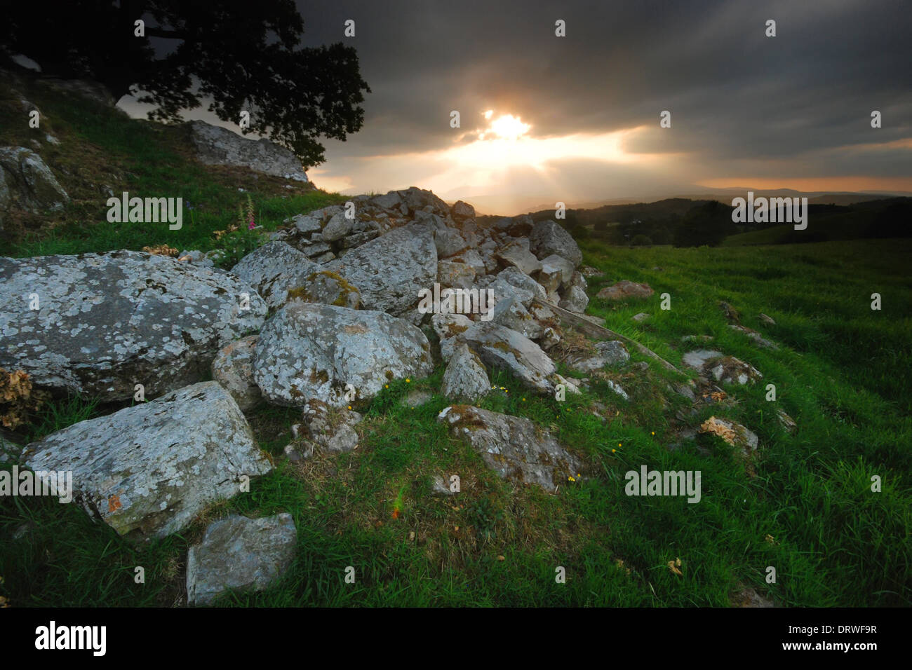 Sun bursting through the clouds, over the North Wales landscape, with rocks in the foreground Stock Photo